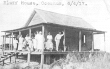 The Bluff House  was an Early Century beach front home,. Photo is dated June 4, 2017 with a family posing on the porch. Photo in black and white.
